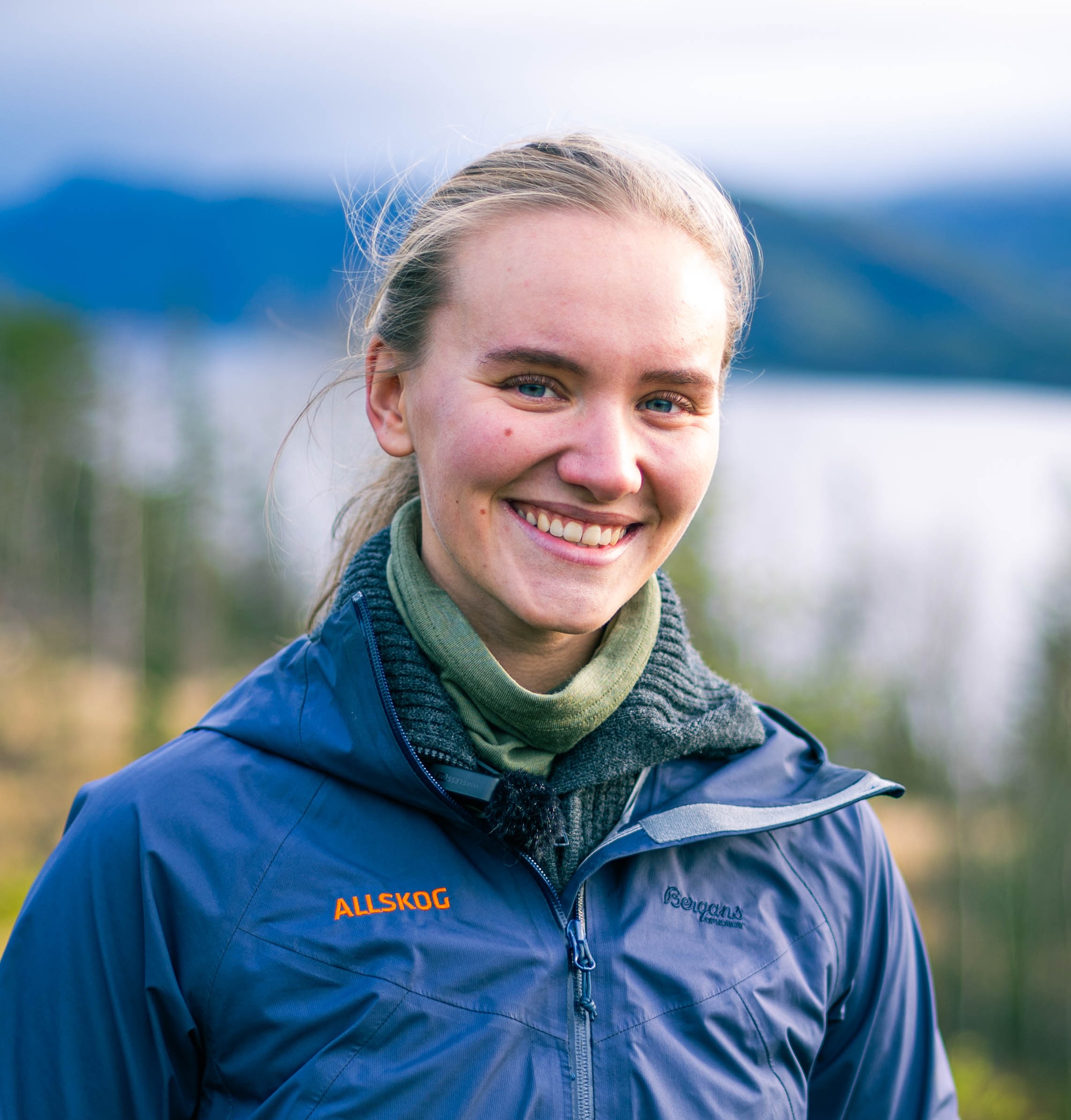 dame med blå jakke står foran en skog