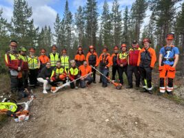 en gjeng ungdommer i arbeidstøy og ryddesager i skogen