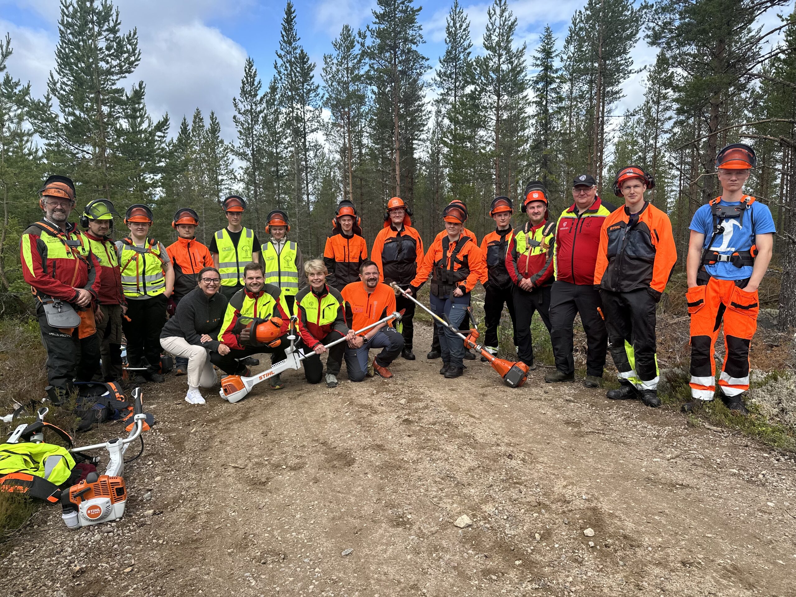 en gjeng ungdommer i arbeidstøy og ryddesager i skogen