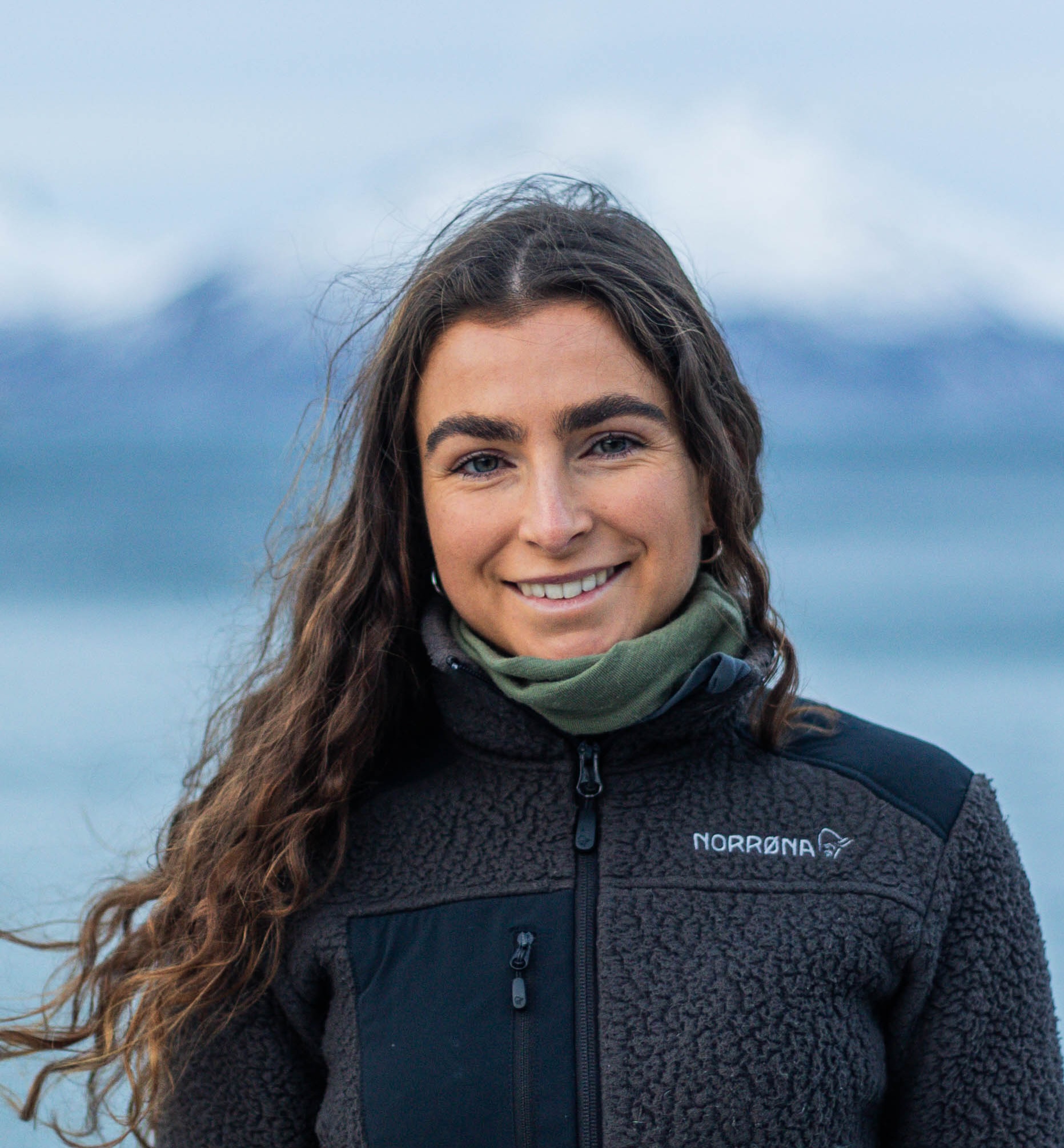 portrett jente med mørkt hår foran fjell og hav